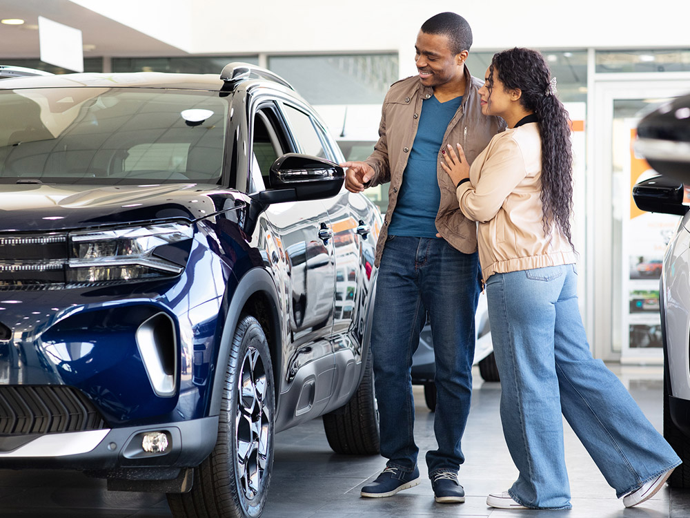 750_0003_iStock-2234180547 A couple looks at a dark blue SUV in a car showroom.