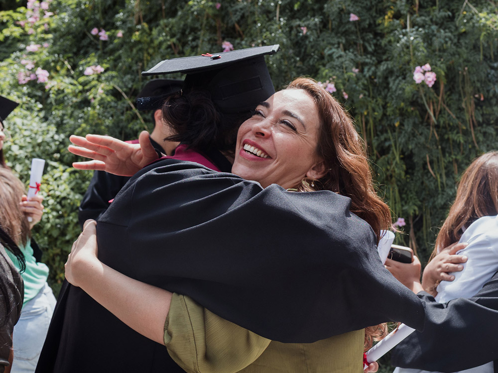 750_0004_iStock-2222463665 Graduate in cap and gown embraces a smiling loved one during an outdoor graduation celebration.