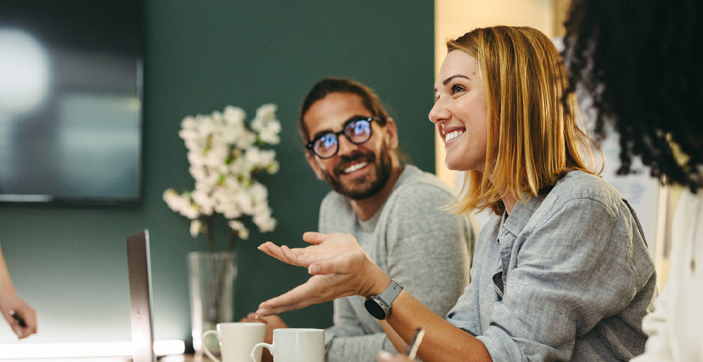 Coworkers smiling and talking together during a meeting around a table.