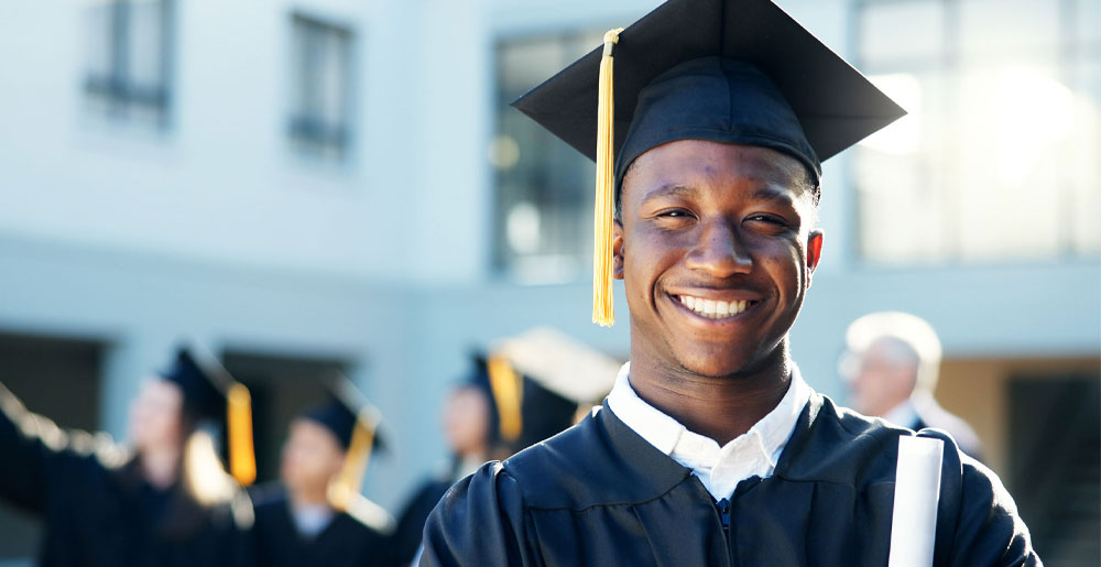 Smiling graduate wearing a cap and gown and holding a diploma.