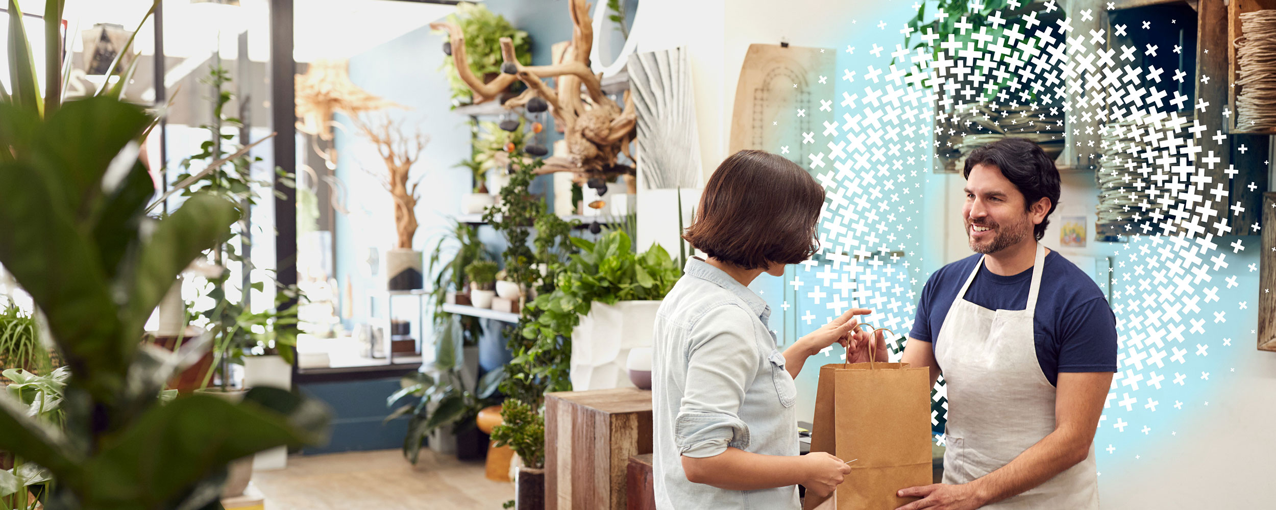 Small business owner handing a shopping bag to a customer inside a plant shop.