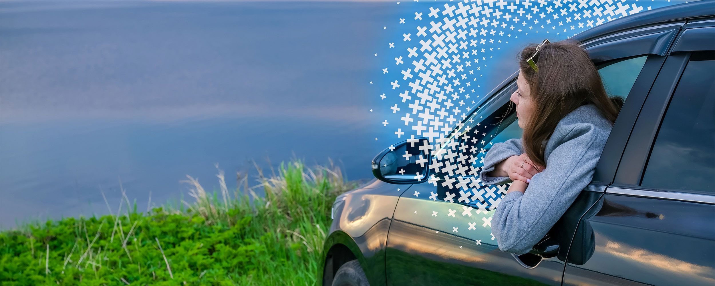 Woman leaning out of a car window while parked beside a scenic body of water.