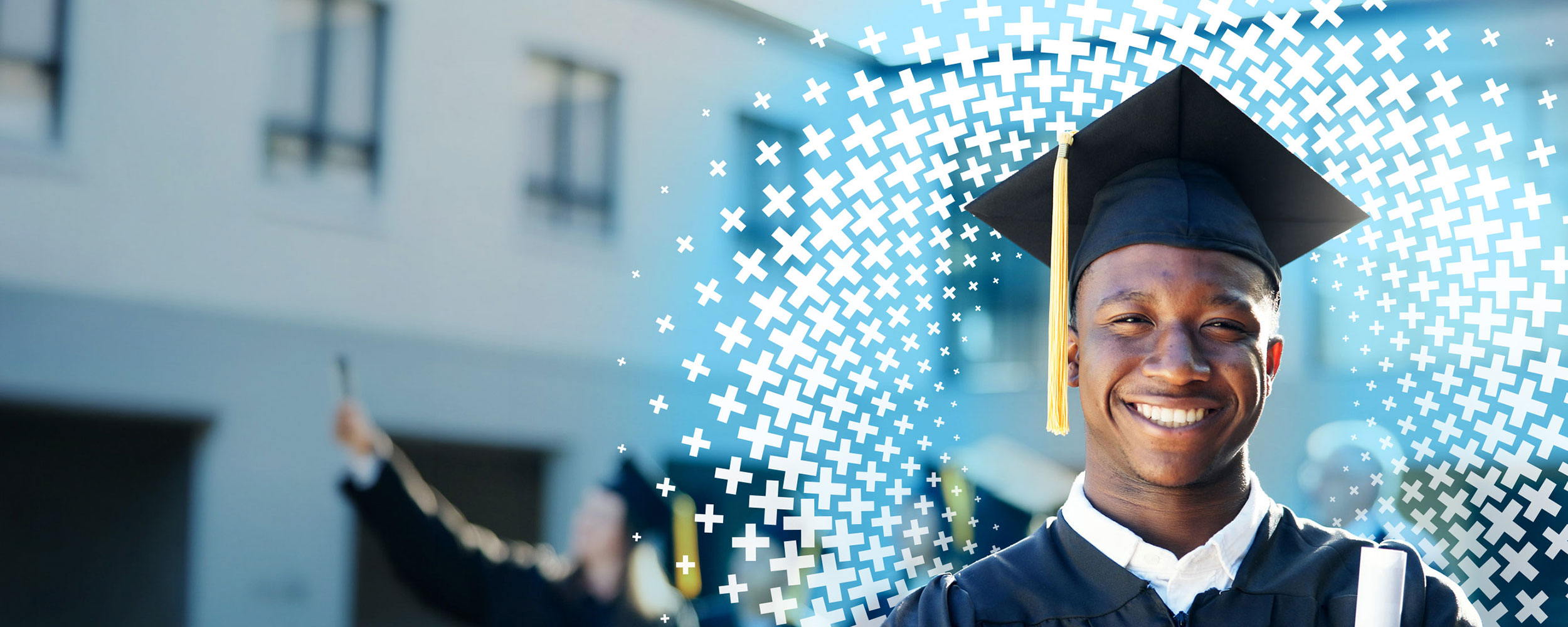 Recent graduate smiles in front of the university building in his cap and gown.