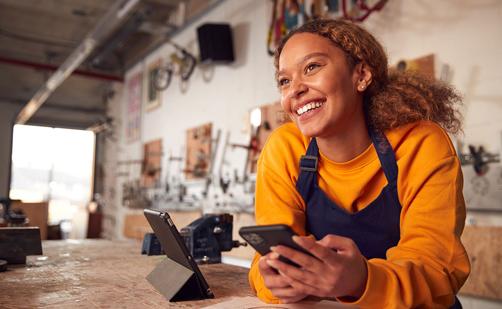 615-bizbankingtools-1716691117 Smiling small business employee wearing an apron in a bright workspace.