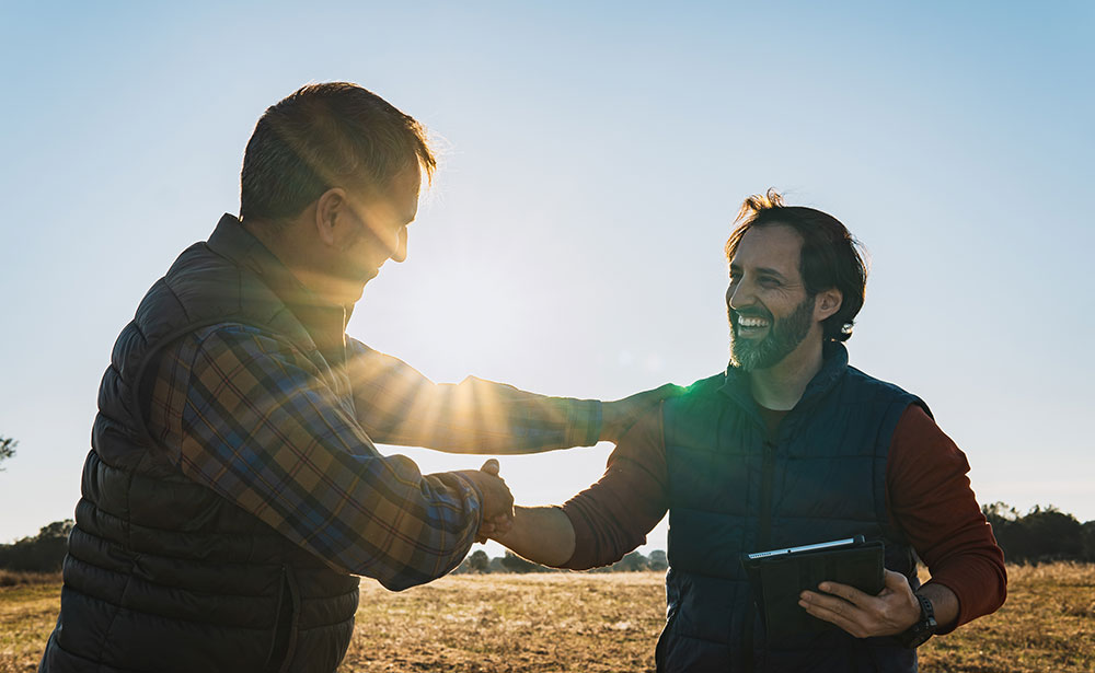 615-bizpartnerprograms-2200131052 Two men shaking hands outdoors during a friendly business conversation.