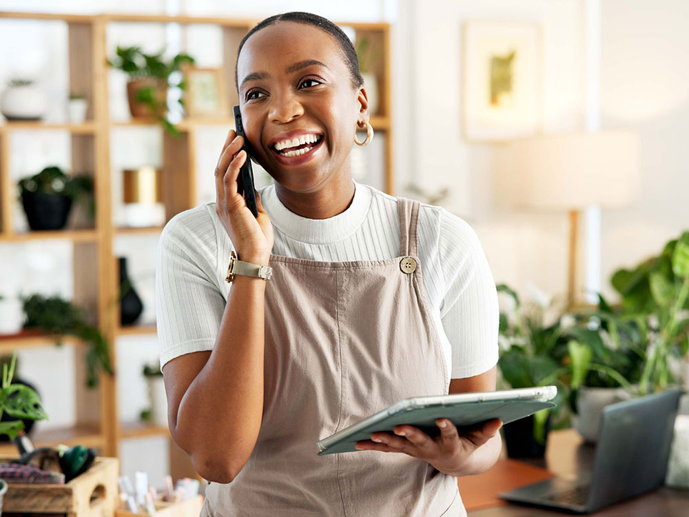 750-bizonline-2251537412 Small business owner talking on a phone while holding a tablet in her shop.