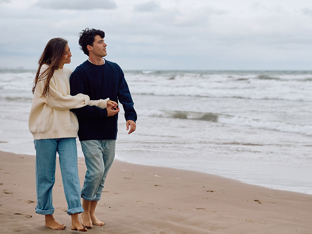 A young couple walks on the beach.
