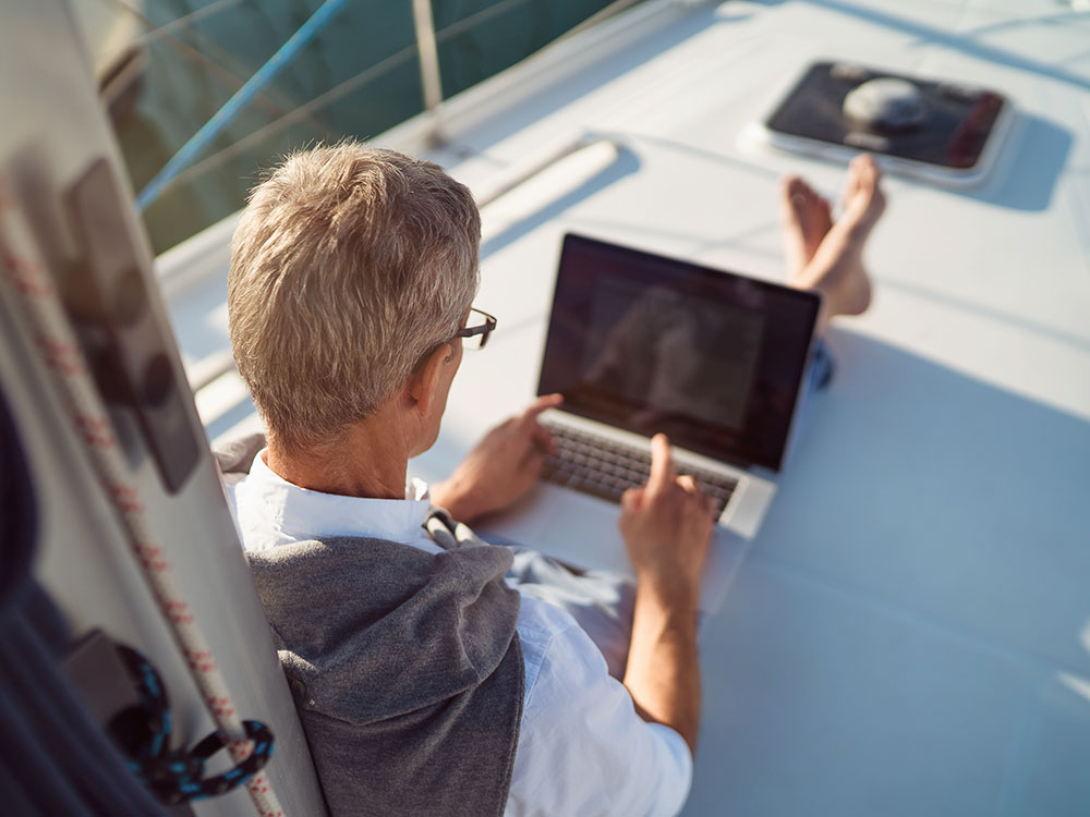 750-online-banking-1308090713 Man works on his laptop while sitting on the bow of his boat.