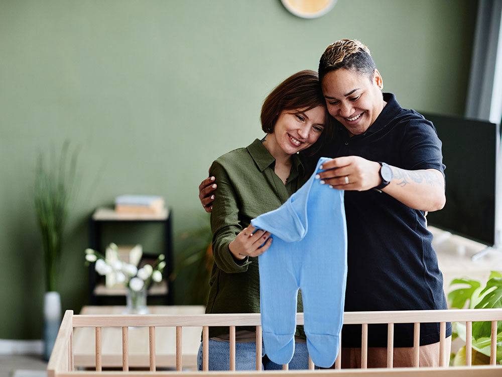750-onlinebanking-1413731372 Two expectant parents holding a blue baby outfit above a crib.