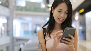 Woman standing in shopping mall using her phone and smiling.