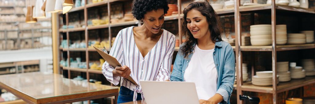 Two business women looking at laptop in storefront.