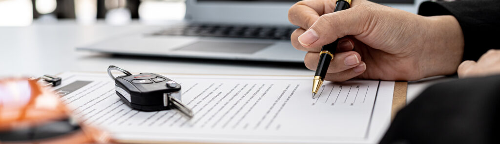 Hand and pen signing a contract in order to purchase a new car.